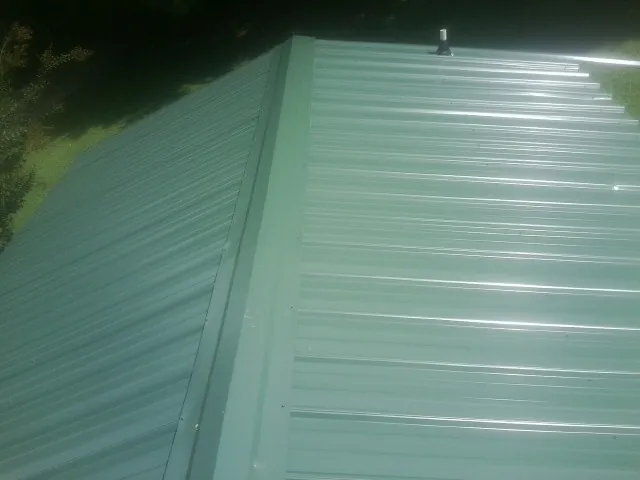 New green metal panels meeting at the ridge of a roof — Flat Roof Repair work by our crew in Ogdensburg