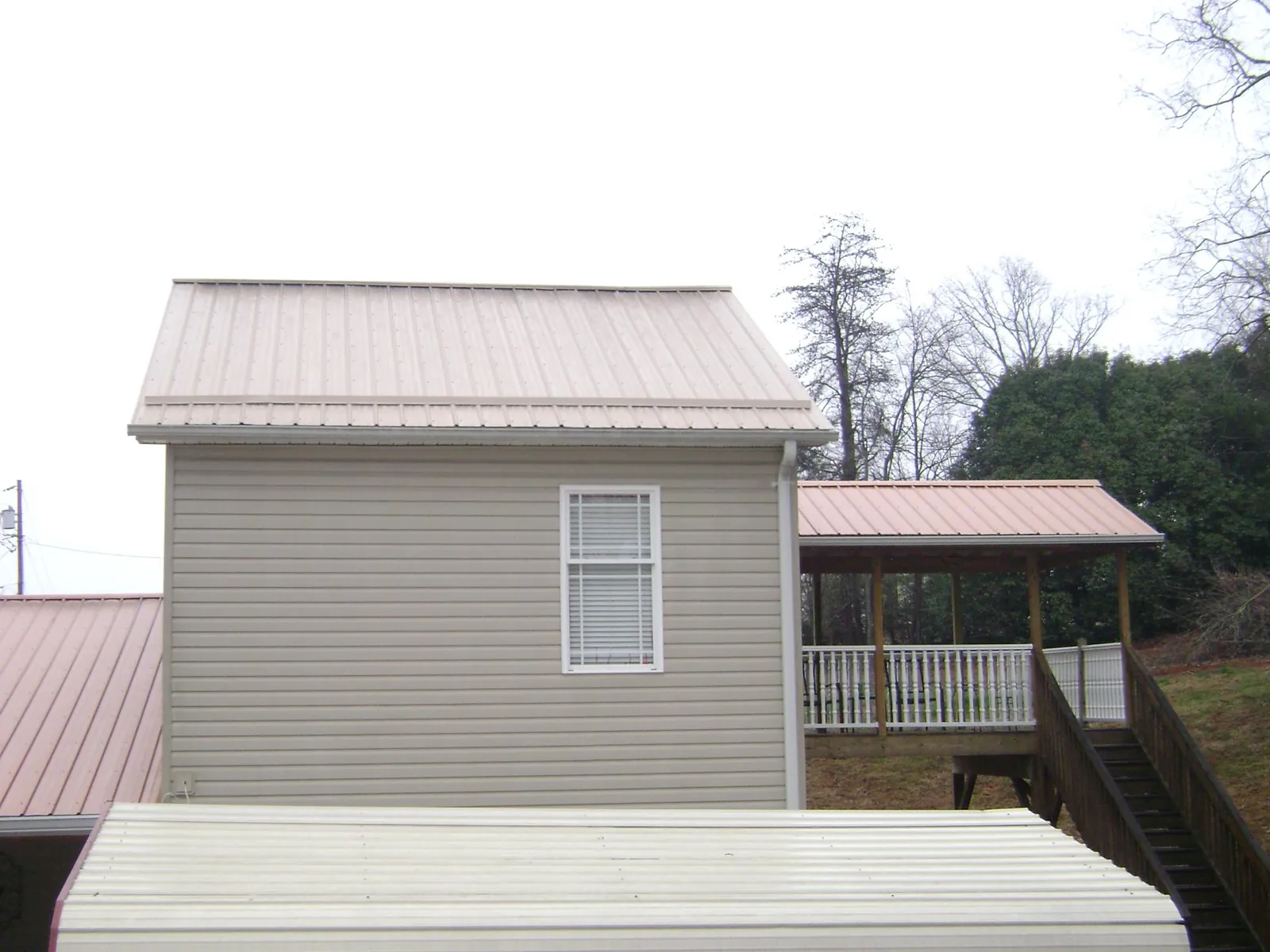 Tan metal roofs on a two story addition and attached porch, from a Roof Replacement job in Ogdensburg
